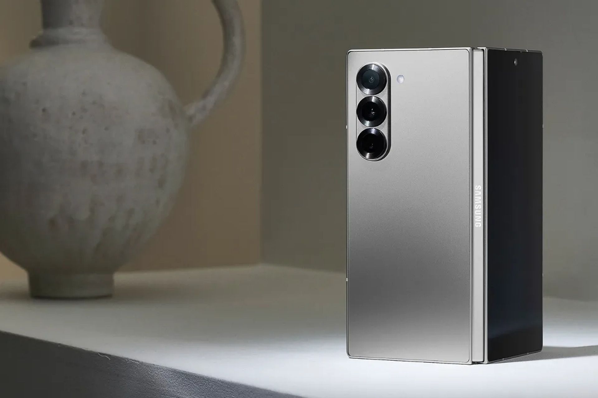 گلکسی زد فولد ۶ نقره‌ای رنگ قرار گرفته روی میز در کنار کوزه