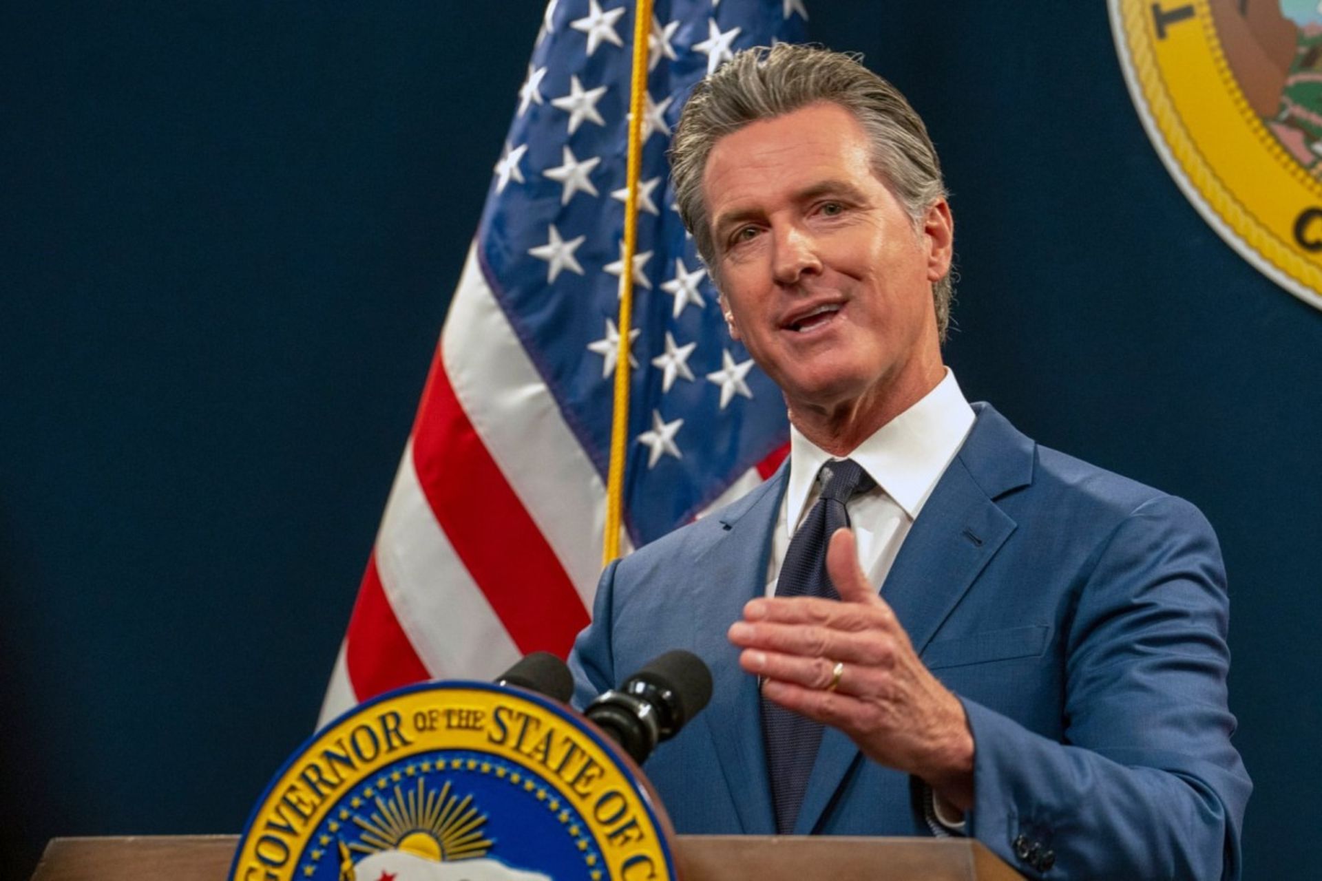 مرد میان‌سال با کت‌شلوار جلو پرچم آمریکا درحال سخنرانی