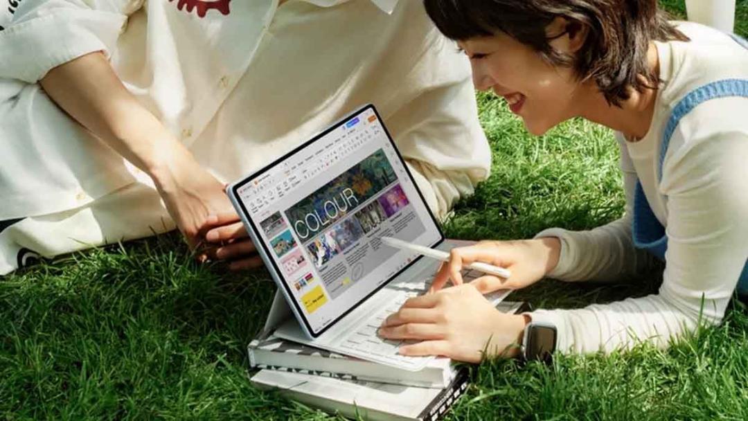 دختری لبخندزنان در فضای باز روی چمن روی یک تبلت در حال طراحی یا ویرایش تصویر است.