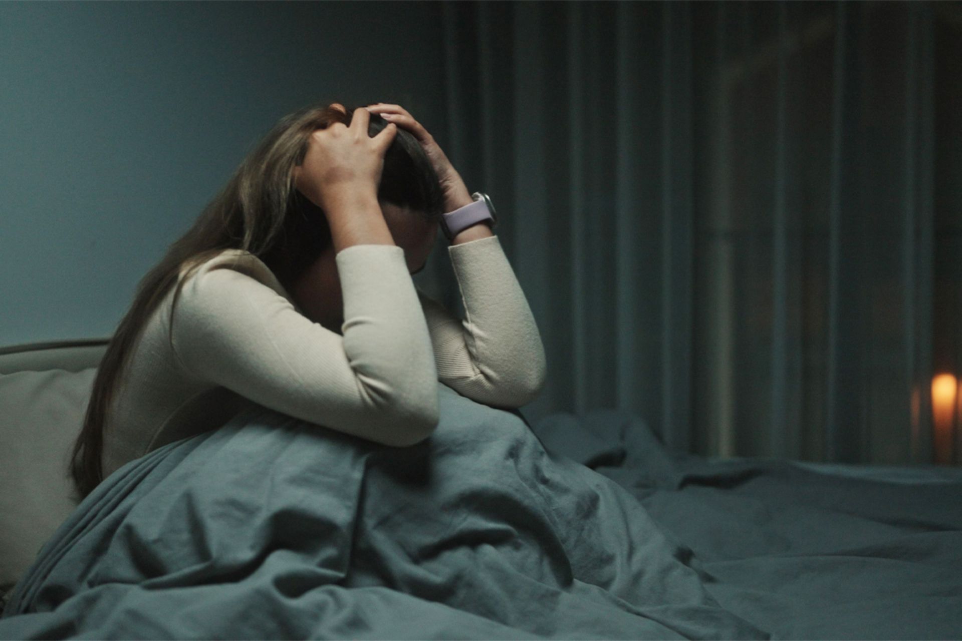 دختری بعد از یک کابوس بیدار شده روی تخت نشسته و سرش را میان دستانش گرفته است