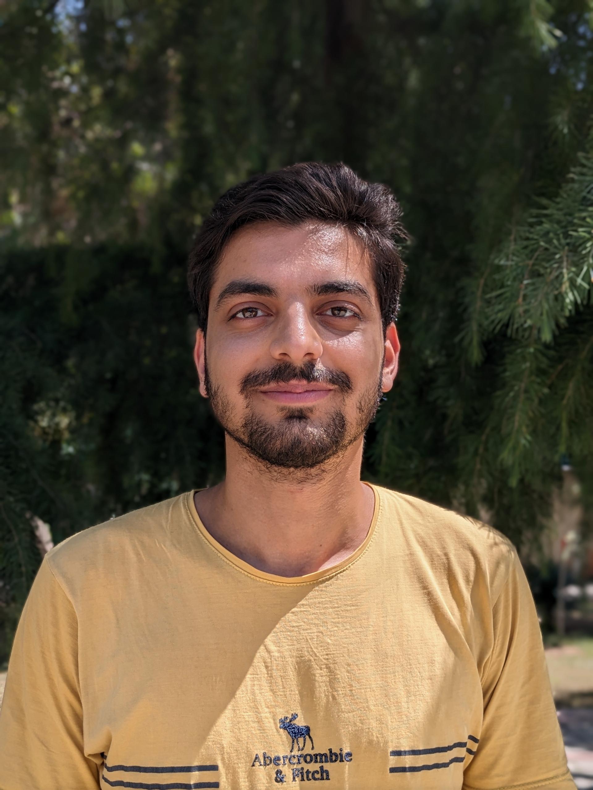 نمونه عکس سلفی پیکسل 8a از یک مرد جوان خوشحال در محیط روشن بیرونی با افکت بوکه