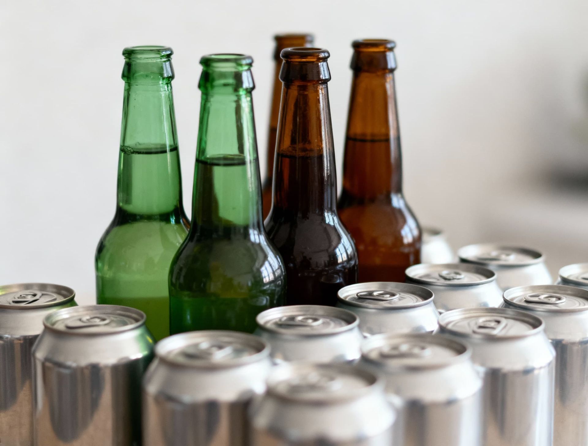 چند بطری شیشه‌ای قهوه‌ای و سبز کنار قوطی‌های آلومینیومی