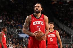 بازیکن تیم راکتس (Houston Rockets) با لباس قرمز در حال کنترل توپ بسکتبال در زمین بازی