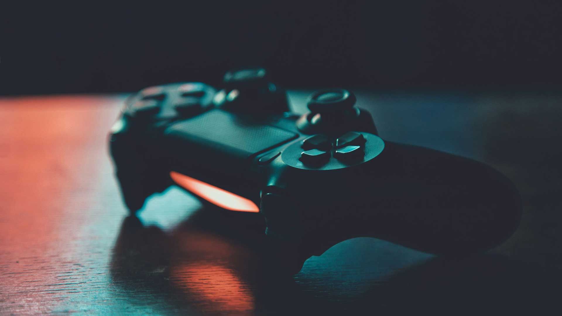 دوال شاک 4، دسته پلی استیشن 4 سونی مشغول ساطع کردن نور نارنجی روی میز داخل اتاق تاریک