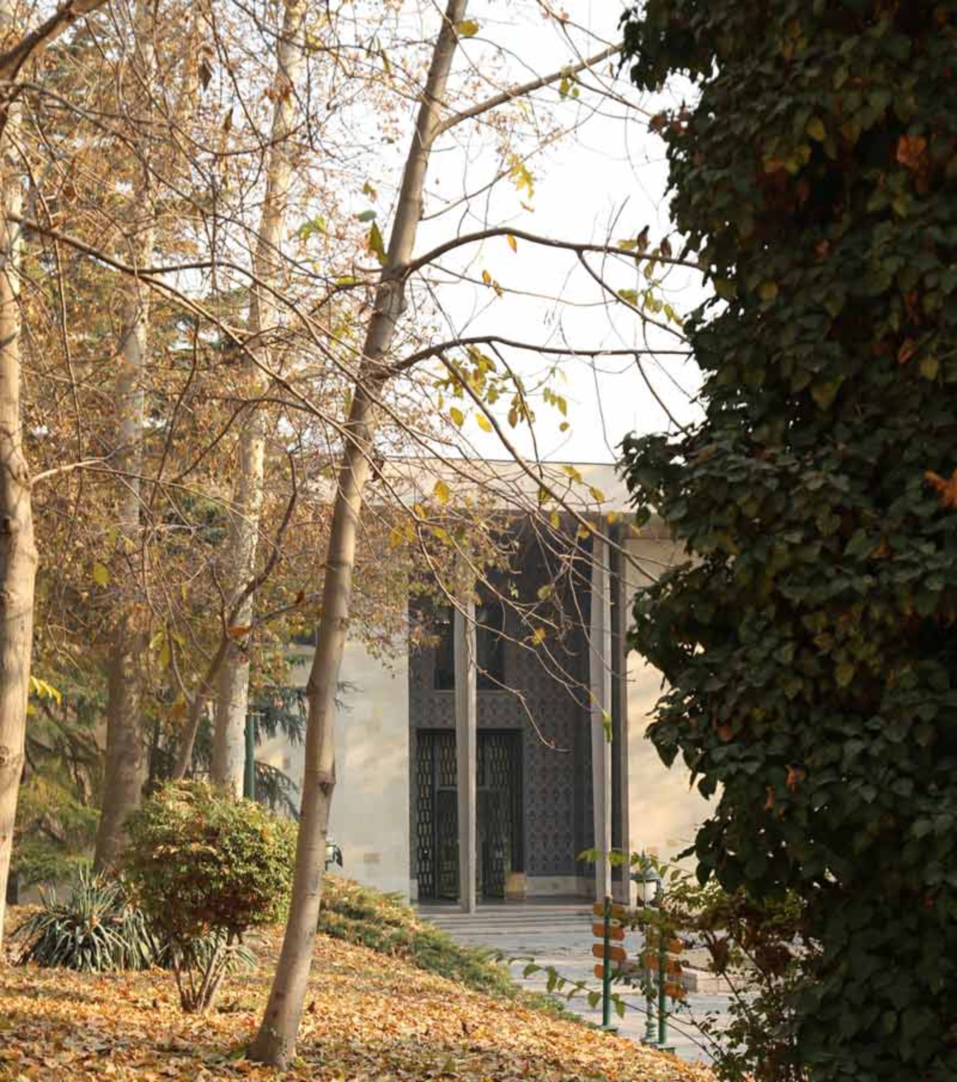 نمایی از ورودی کاخ نیاوران در میان درختان باغ نیاوران در پاییز