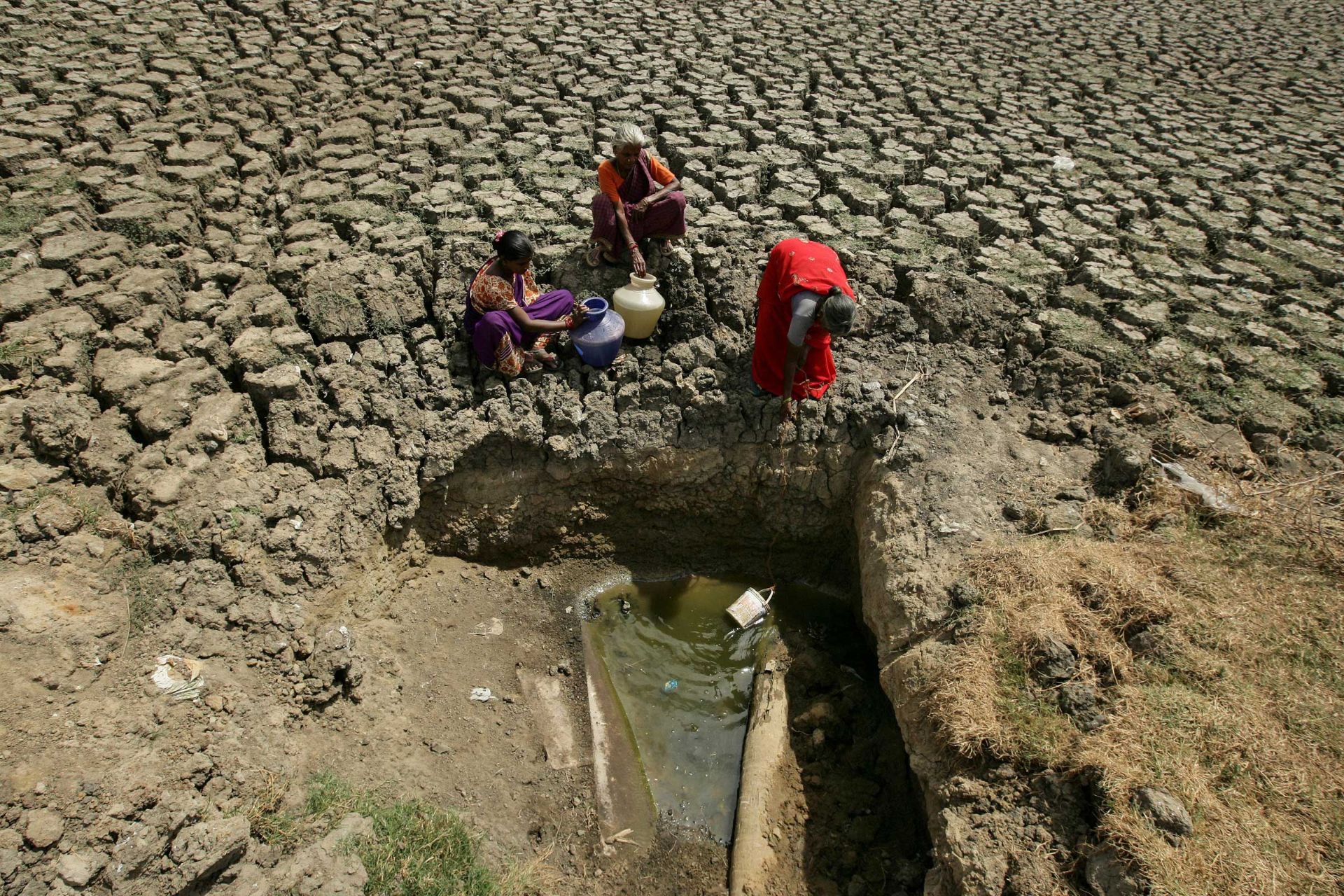 سه زن در هند در تلاش برای پرکردن ظرف‌های آب خود از چشمه