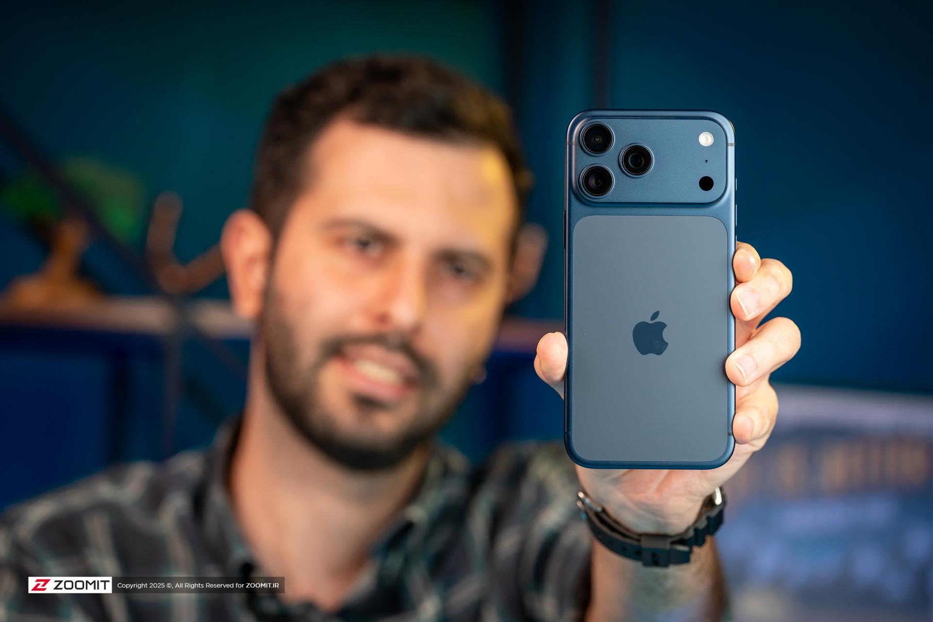 نمای پشت گوشی آیفون ۱۷ پرو مکس / iPhone 17 Pro Max در دست چپ مرد جوان ریشی