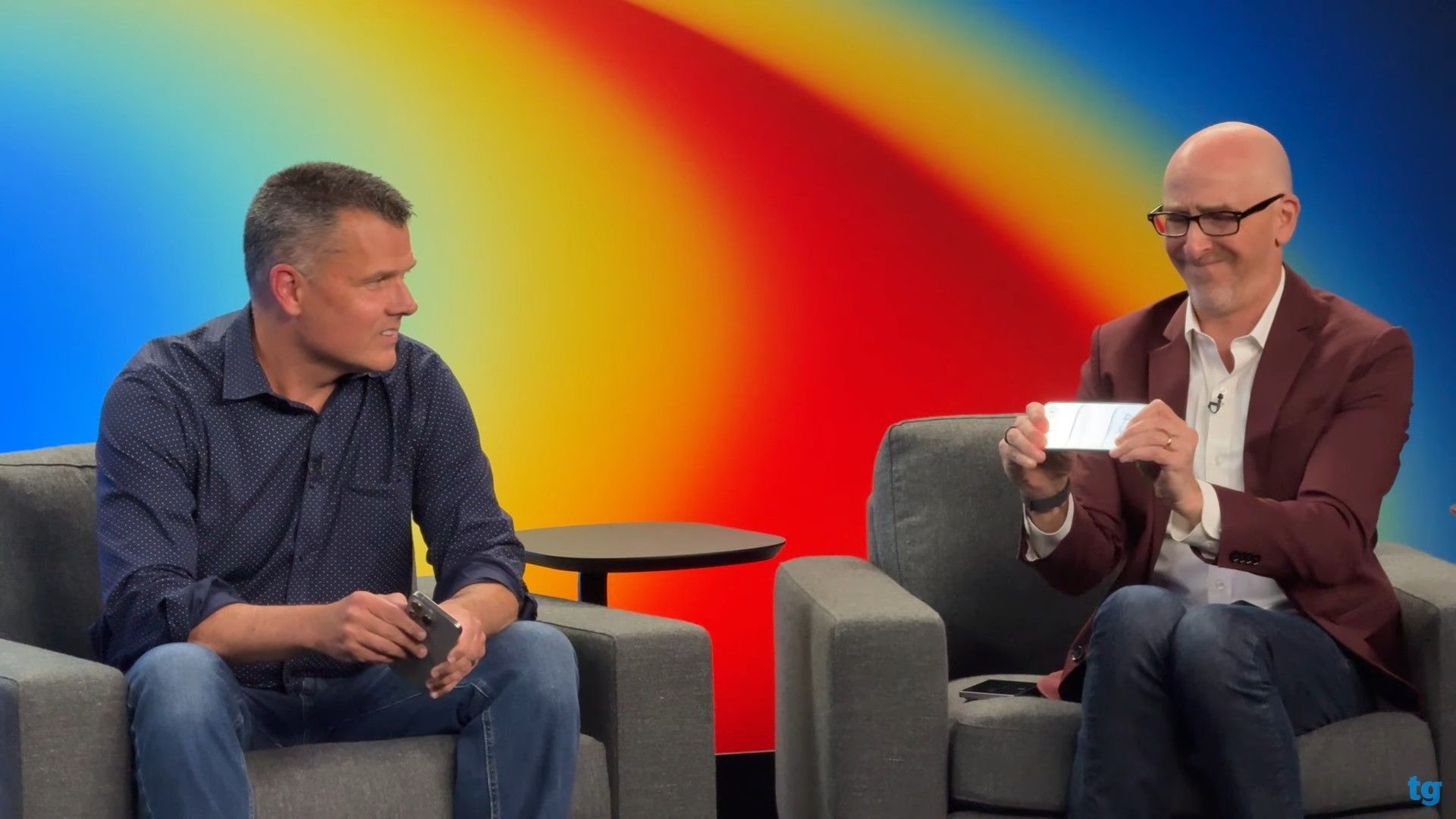 دو مرد کنار هم نشسته در حال خم‌کردن یک گوشی