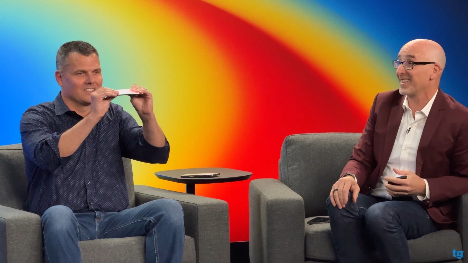 دو مرد کنار هم نشسته در حال خم‌کردن یک گوشی