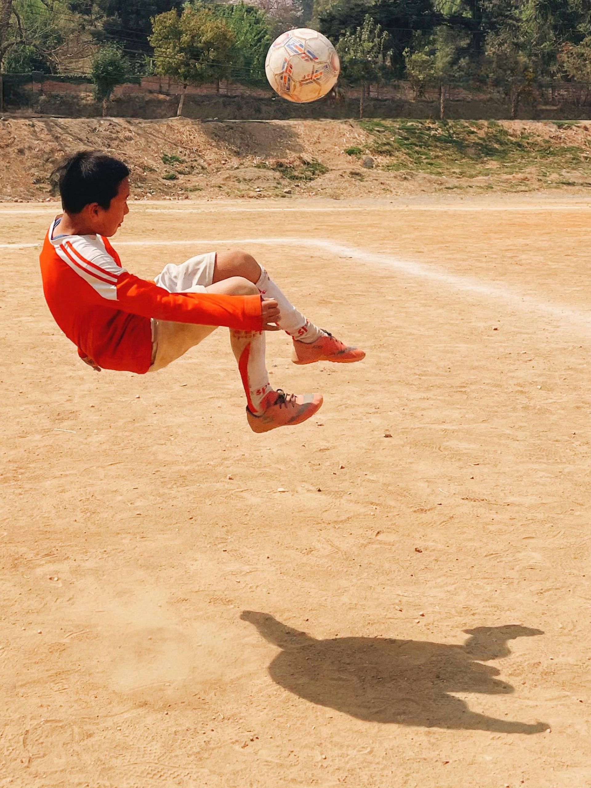 پسر بچه درحال برگردون زدن در زمین فوتبال خاکی