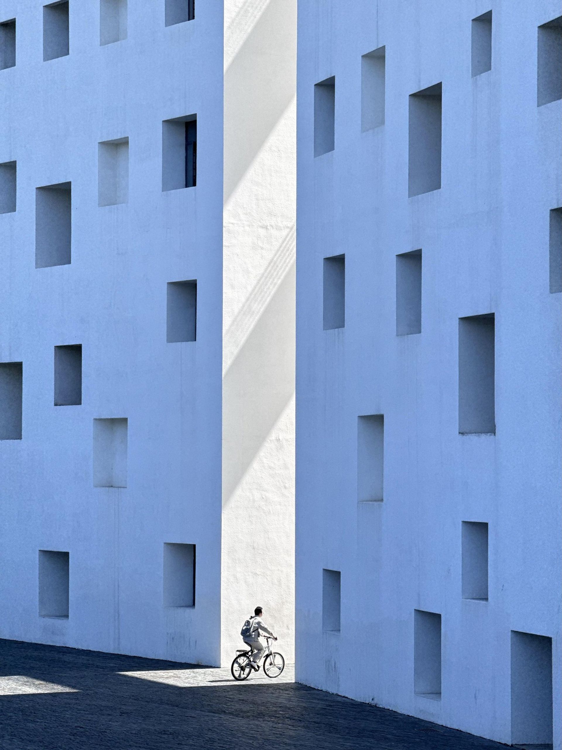 مرد درحال دوچرخه سواری و رفتن به کوچه میان ساختمان های آبی