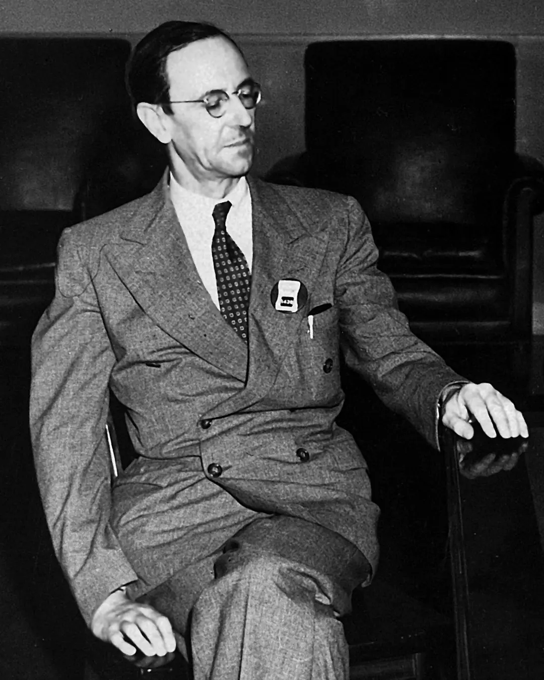 جیمز چادویک (James Chadwick) با عینک و کت رسمی نشسته است