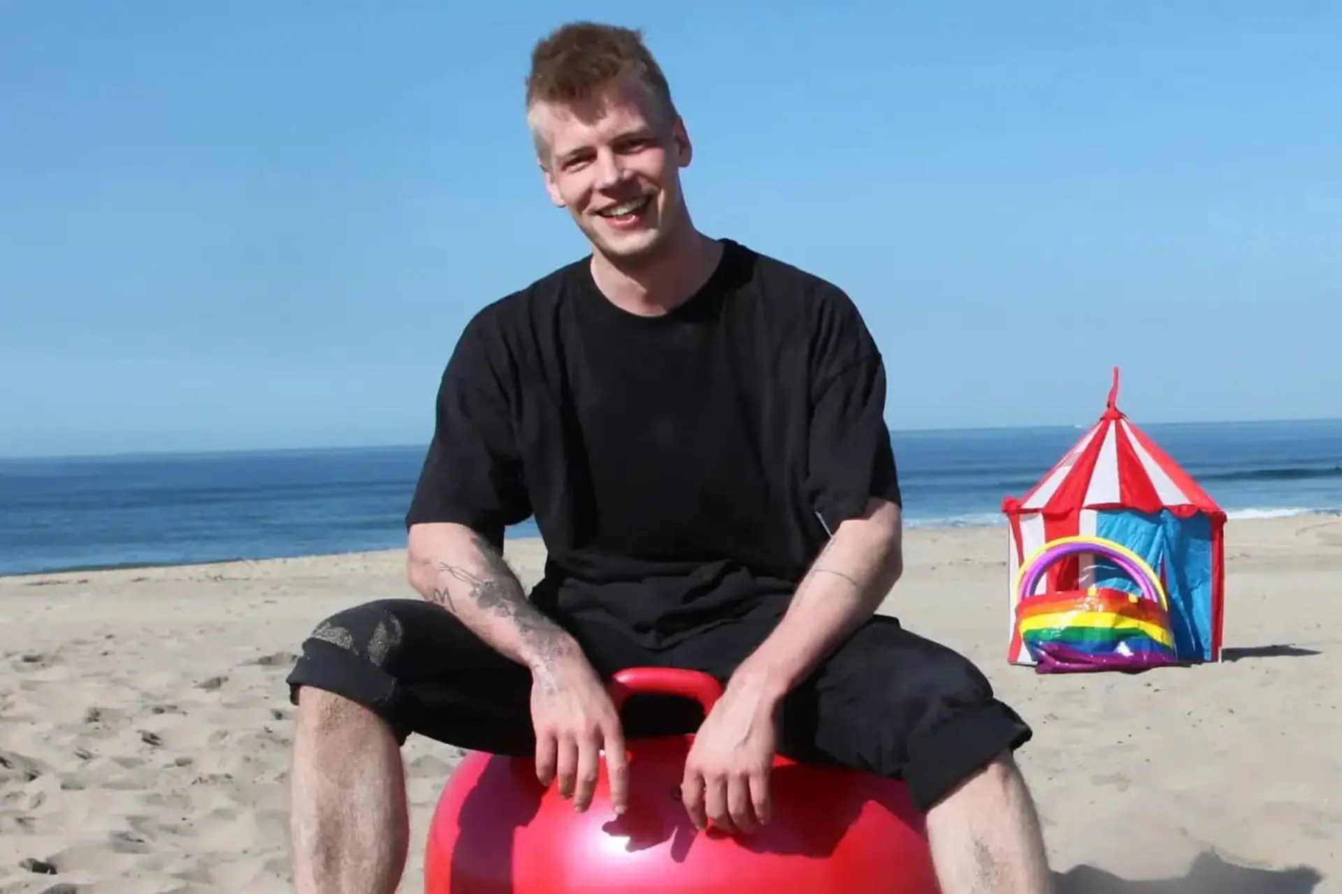 مرد جوانی با خنده روی توپی در ساحل نشسته. جیمی پارکینن و کیل ایلان ماسک