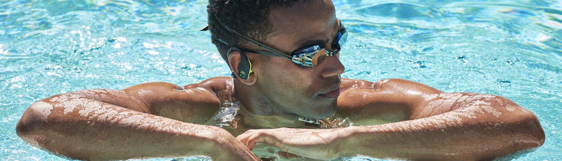 شناگر مرد با هندزفری جی بی ال و عینک مخصوص شنا درون آب
