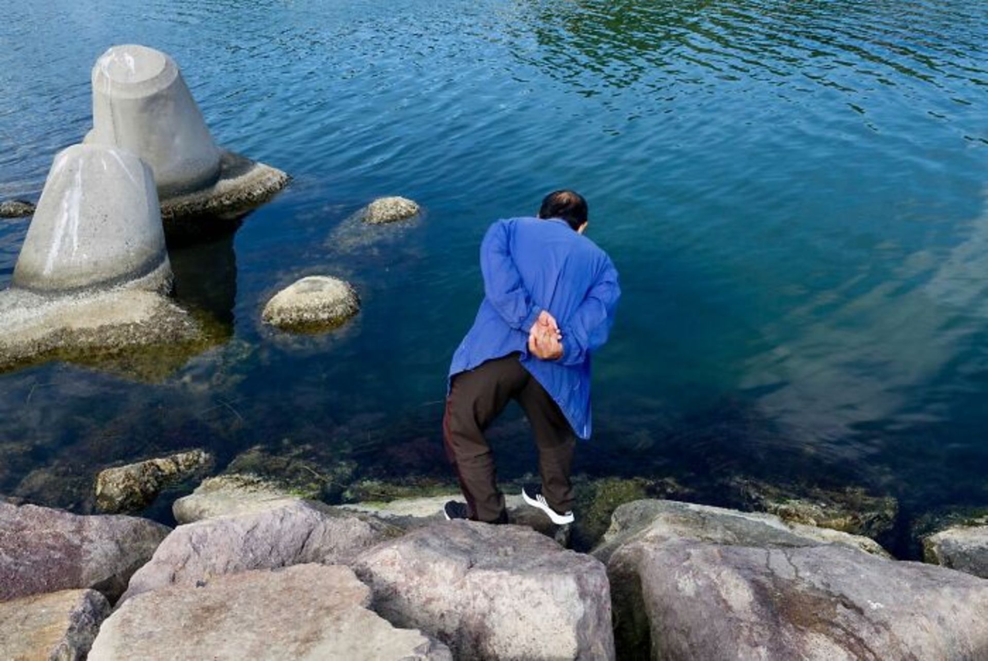 مرد خم شده و به داخل آب نگاه می‌کند