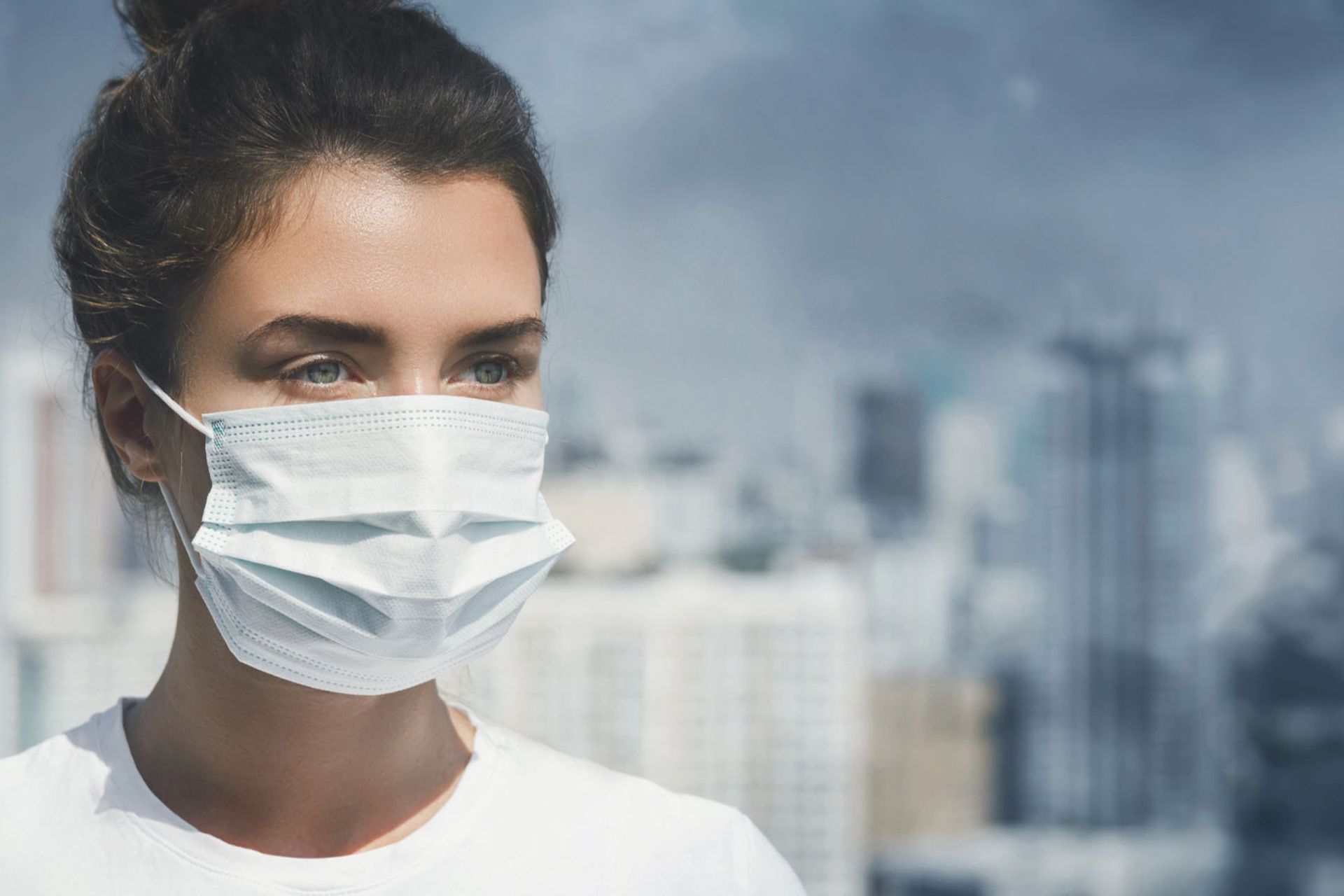 زن دارای ماسک در پس‌زمینه شهر آلوده