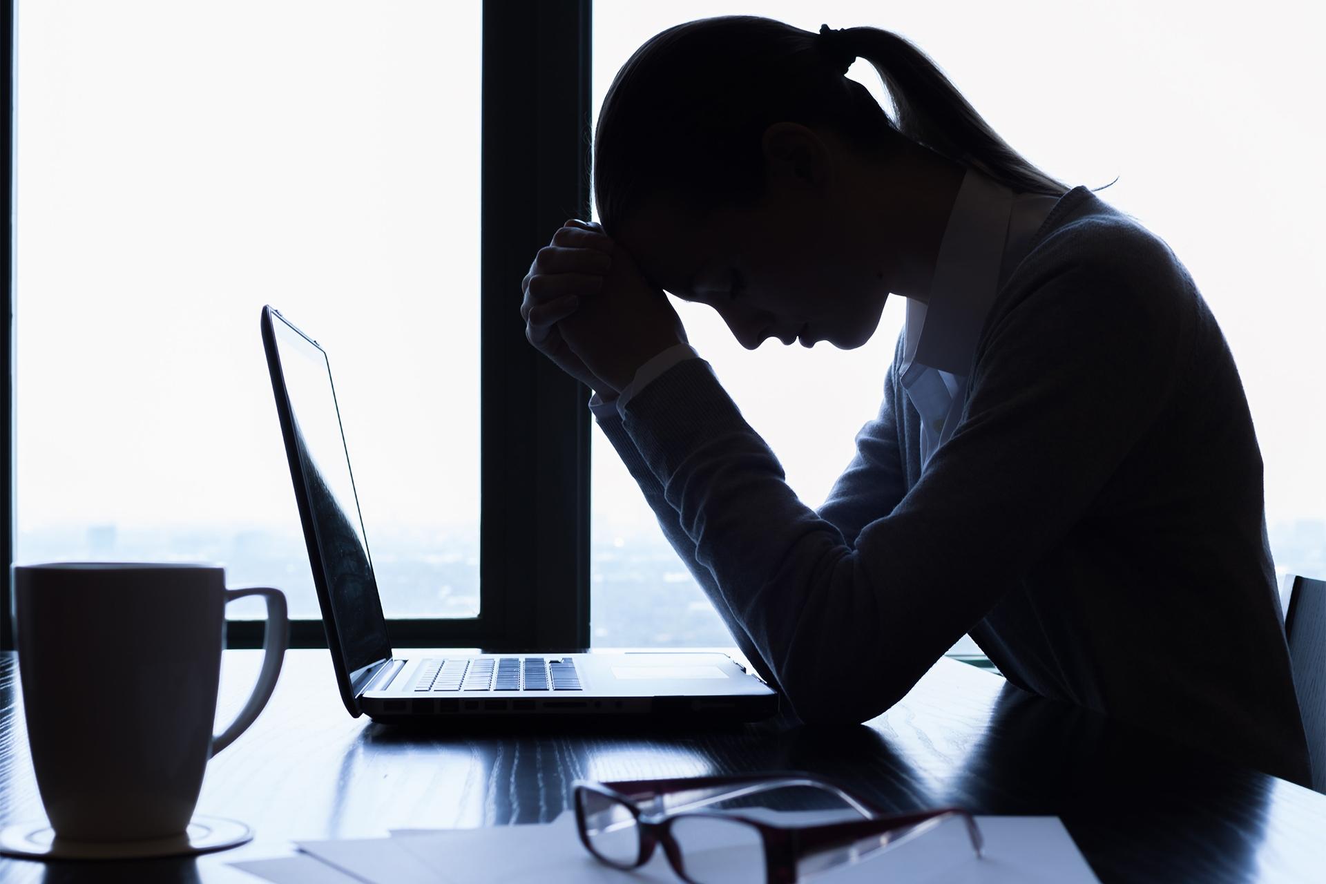 زن غمگین جلو لپ‌تاپ با دست روی پیشانی