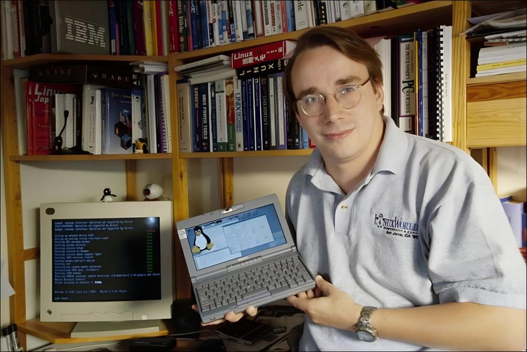  لینوس توروالدز و لینوکس (Linux) روی نمایشگر یک لپ‌تاپ قدیمی در کنار مانیتور کامپیوتر