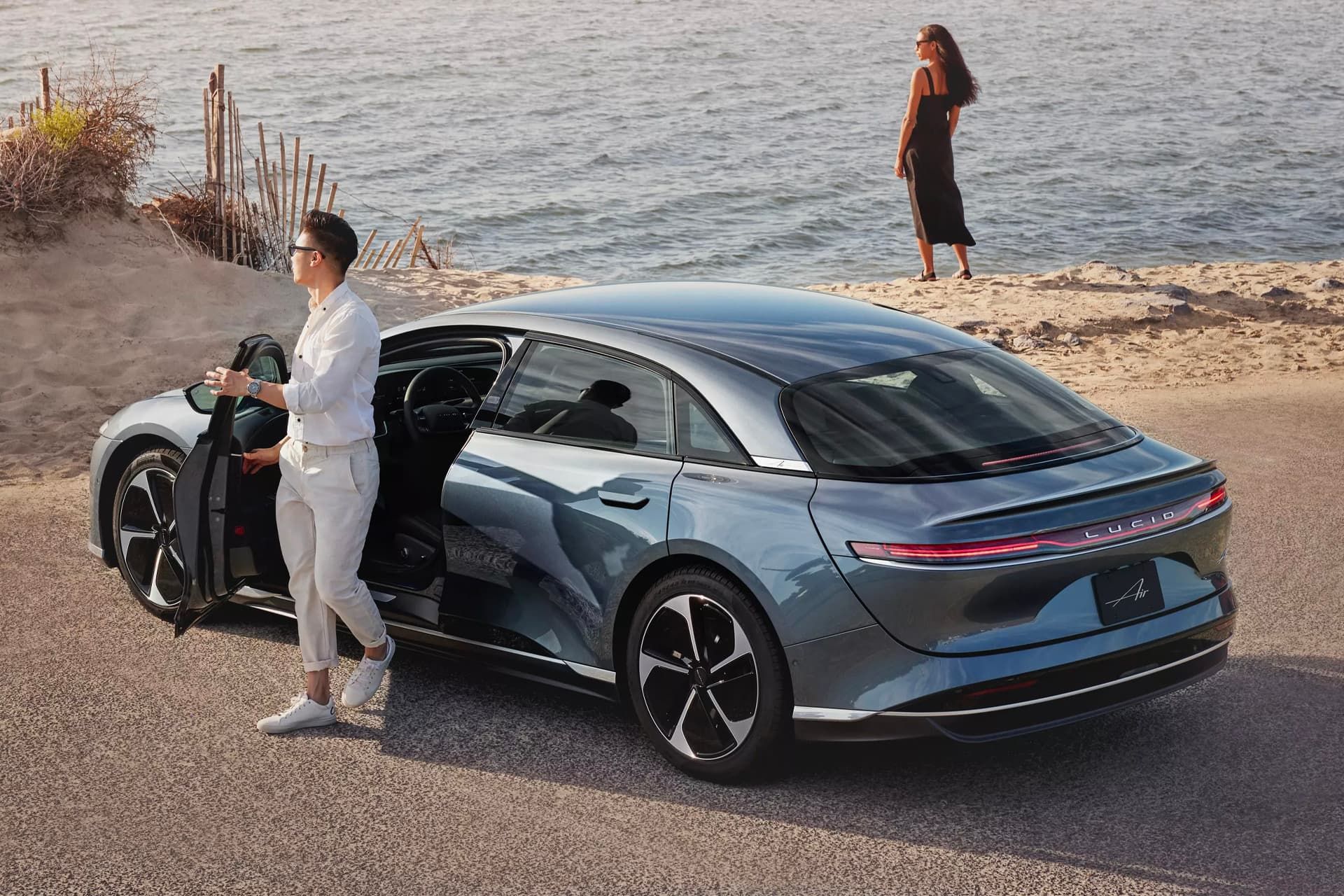 مرد و زن جوان در کنار خودرو لوسید Lucid Air Pure RWD در ساحل