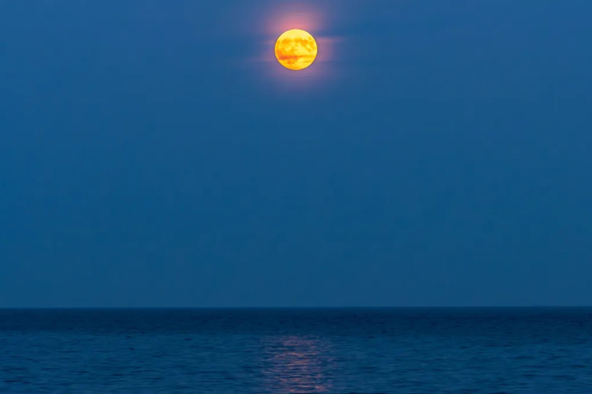 ماه کامل شیری رنگ در آسمان آبی بالای دریا