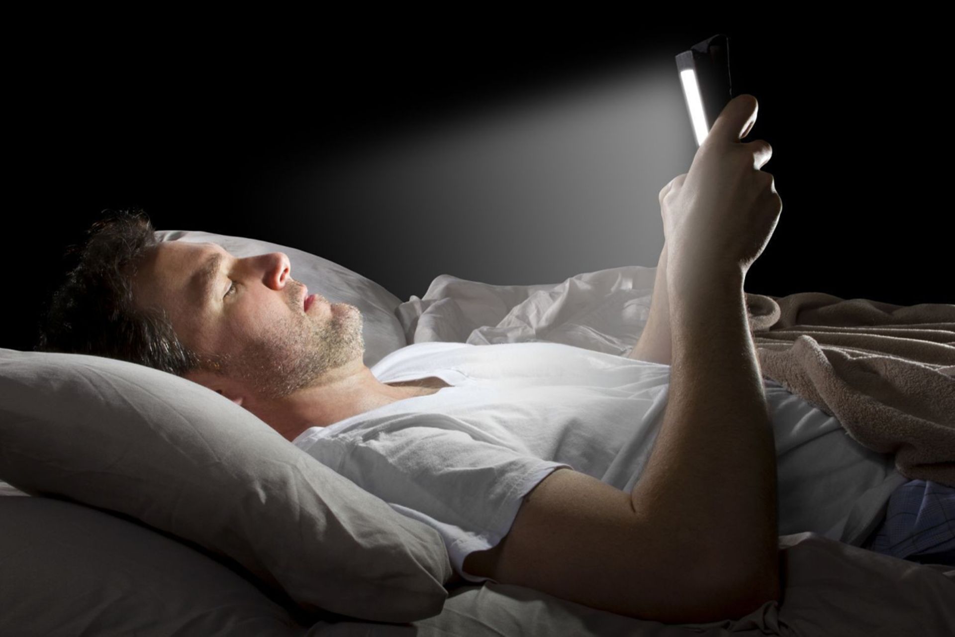 مردی در حال نگاه کردن به گوشی همراه در رخت خواب