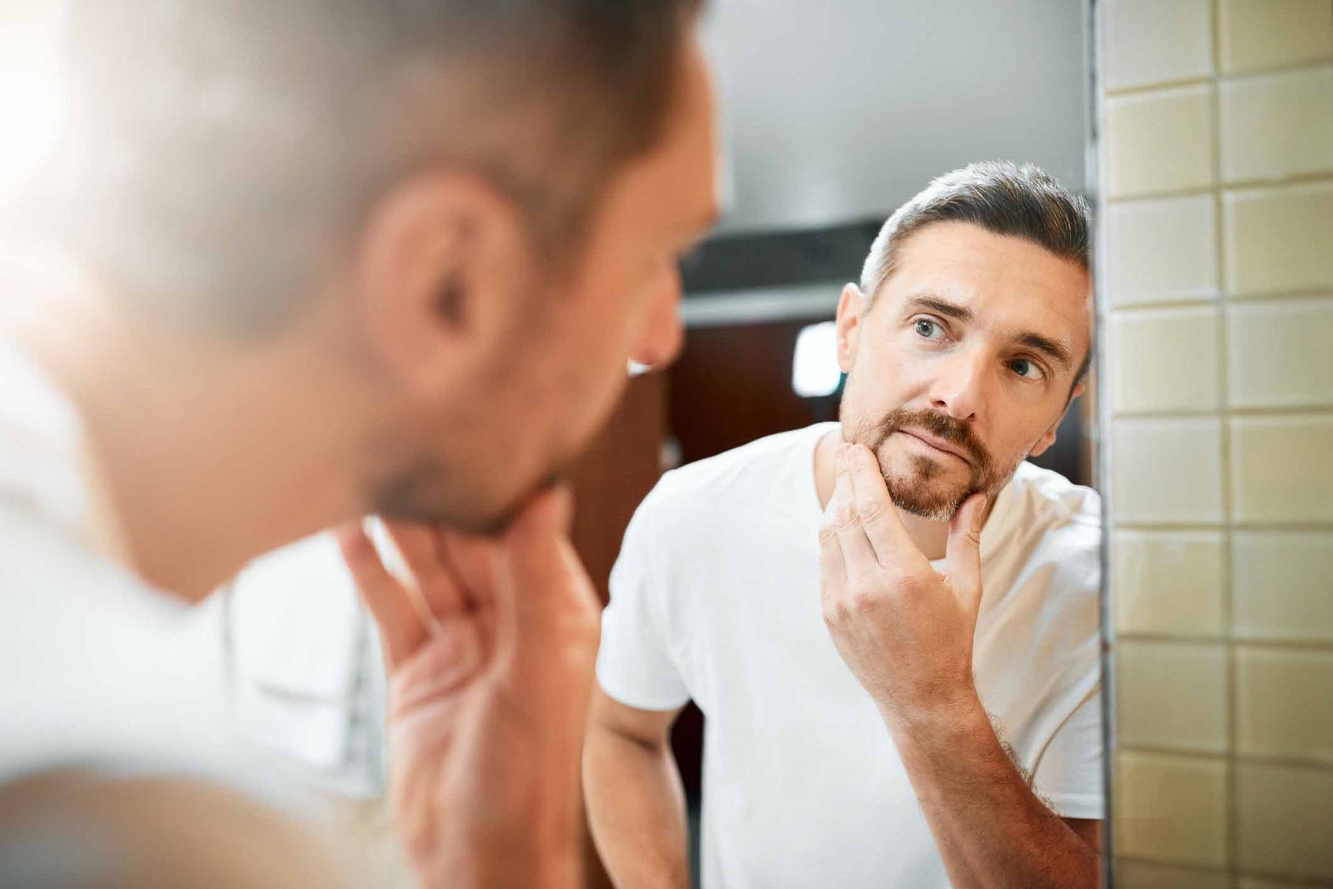 مرد جوان به موهای سفید خود در آینه نگاه می‌کند