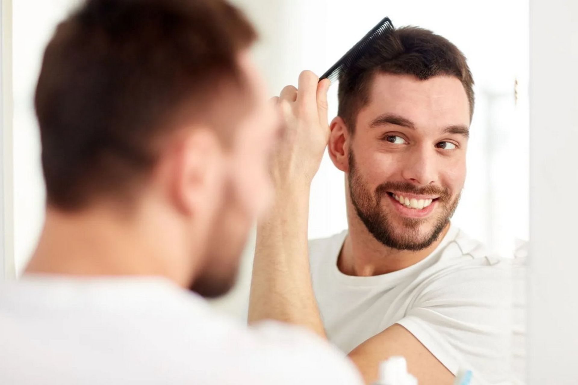 مردی با لبخند در حال شانه کردن موها جلوی آینه