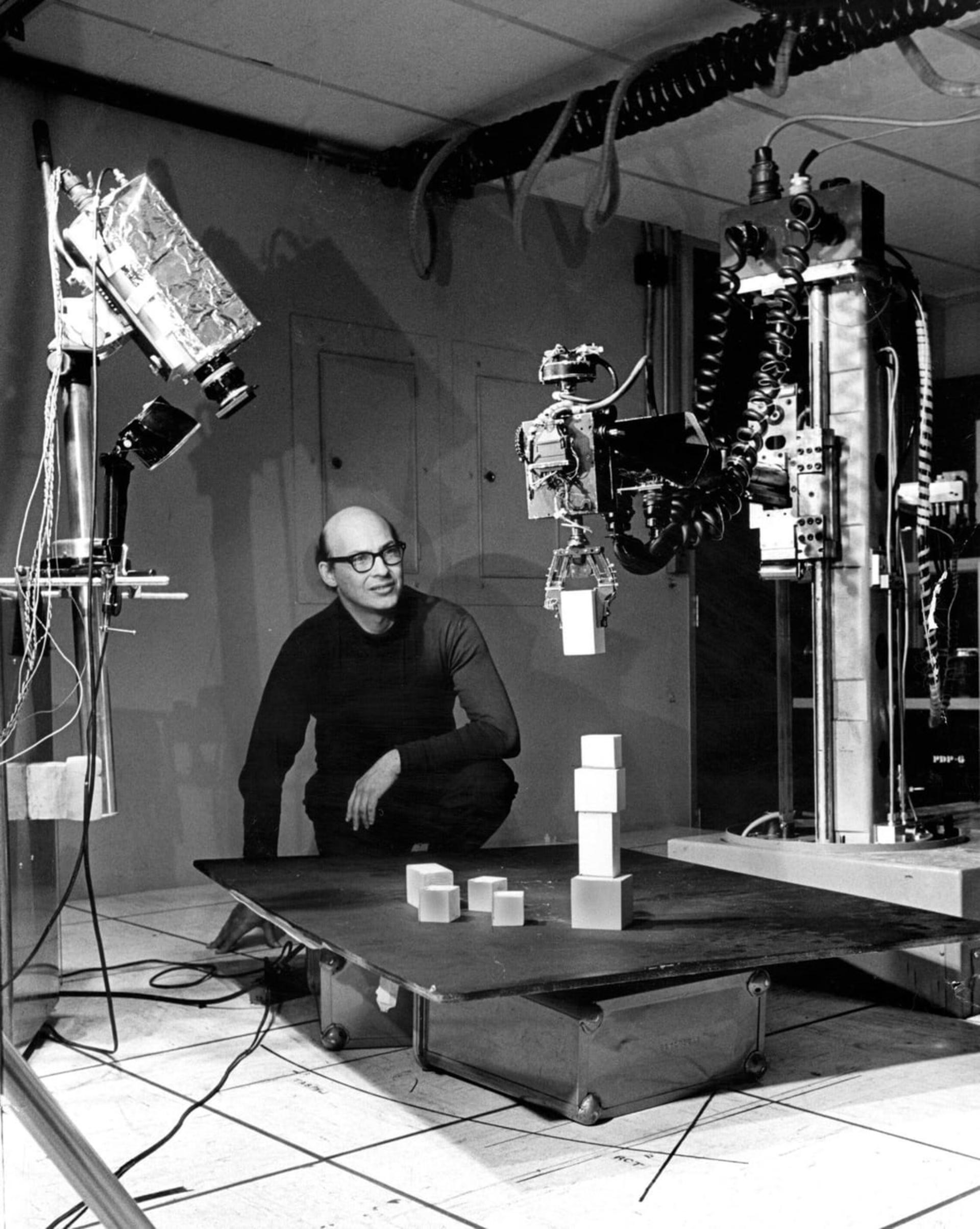 ماروین مینسکی (Marvin Minsky) در کنار تجهیزات رباتیک و مکعب‌های آزمایشی