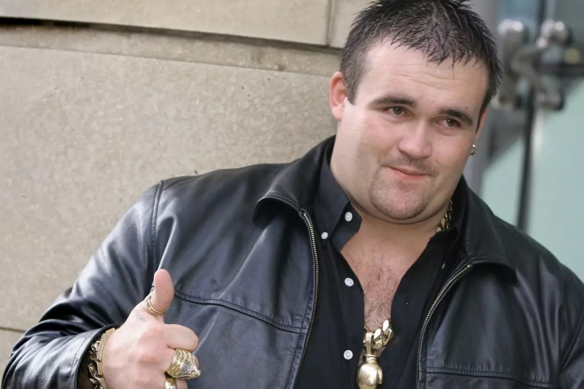 مردی با کت چرمی مشکی و زنجیر و انگشتر طلا به دست