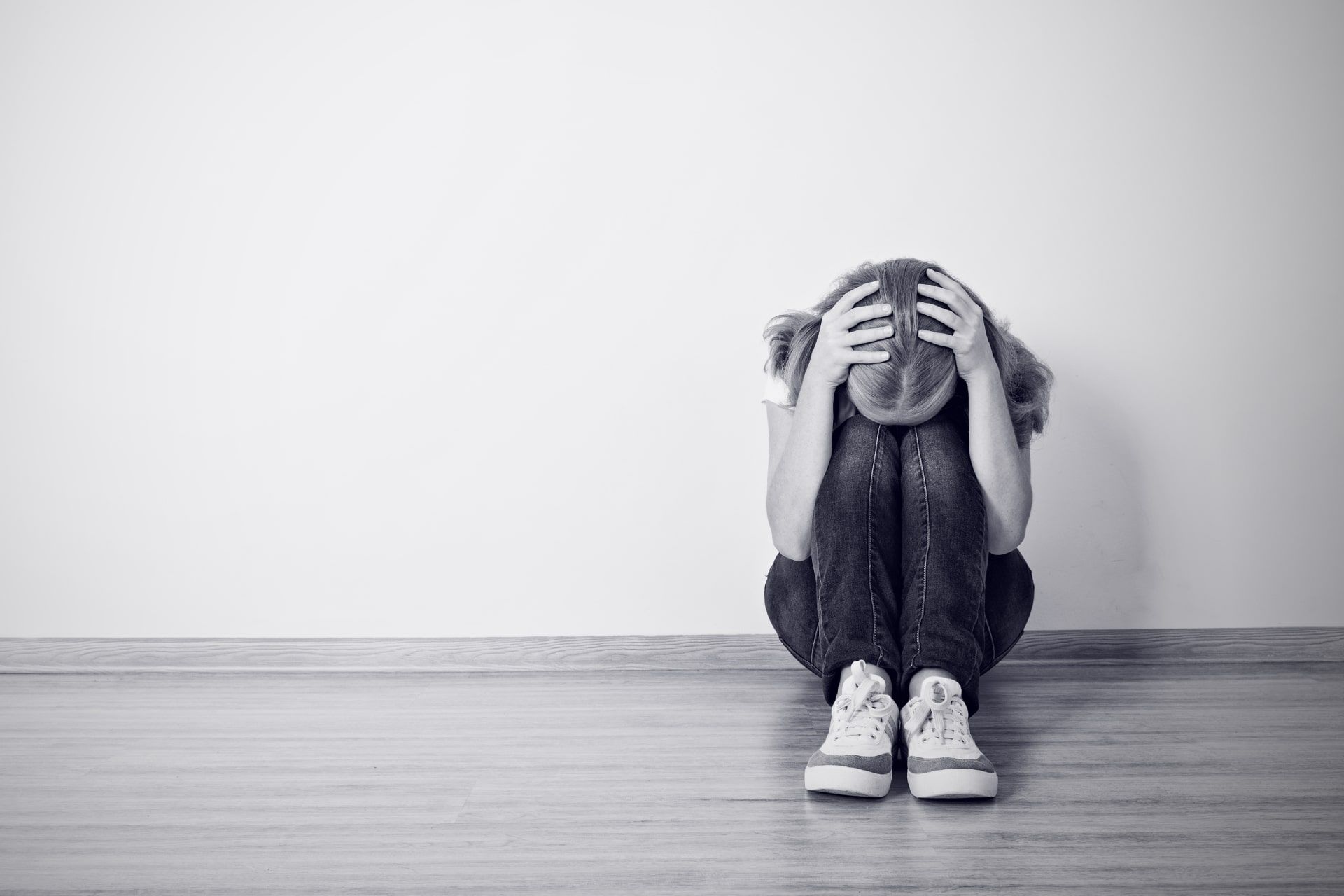 دختری که روی زمین نشسته و سرش را در دست گرفته خاکستری