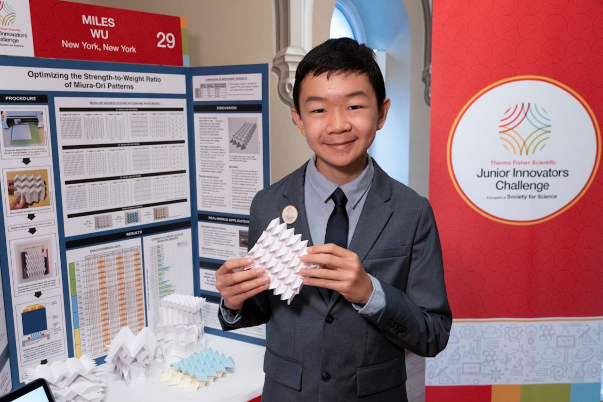 مایلز وو با کت‌وشلوار و با اوریگامی در دست