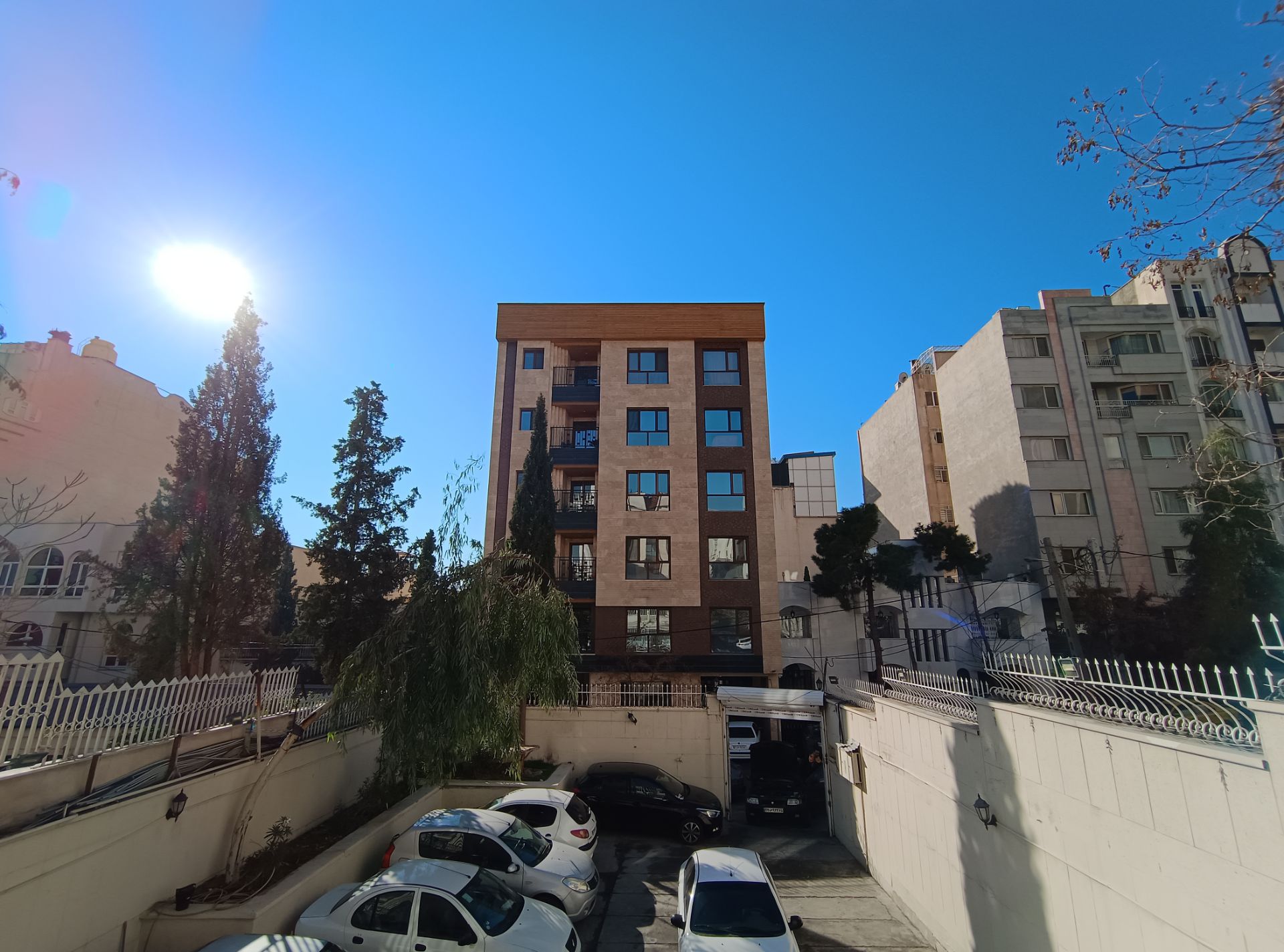 ساختمان در وسط و درختان و خورشید در سمت چپ