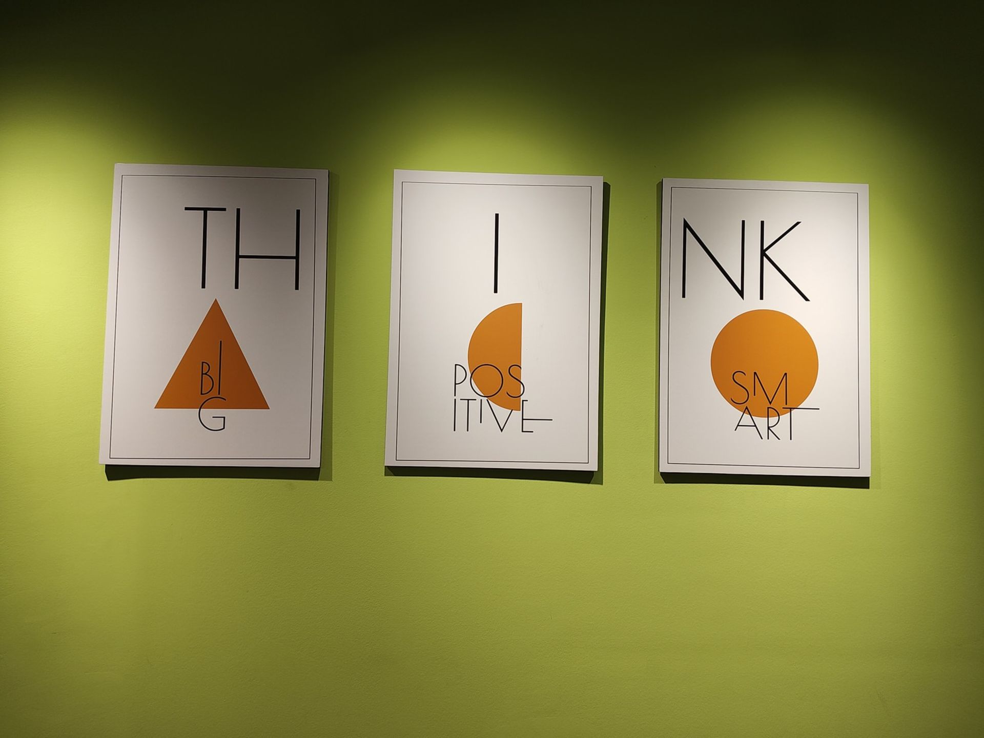 نمونه عکس ریزر ۴۰ اولترا از چند تابلو با طراحی مینیمال روی دیواری سبز رنگ در محیط داخلی یک دفتر کار