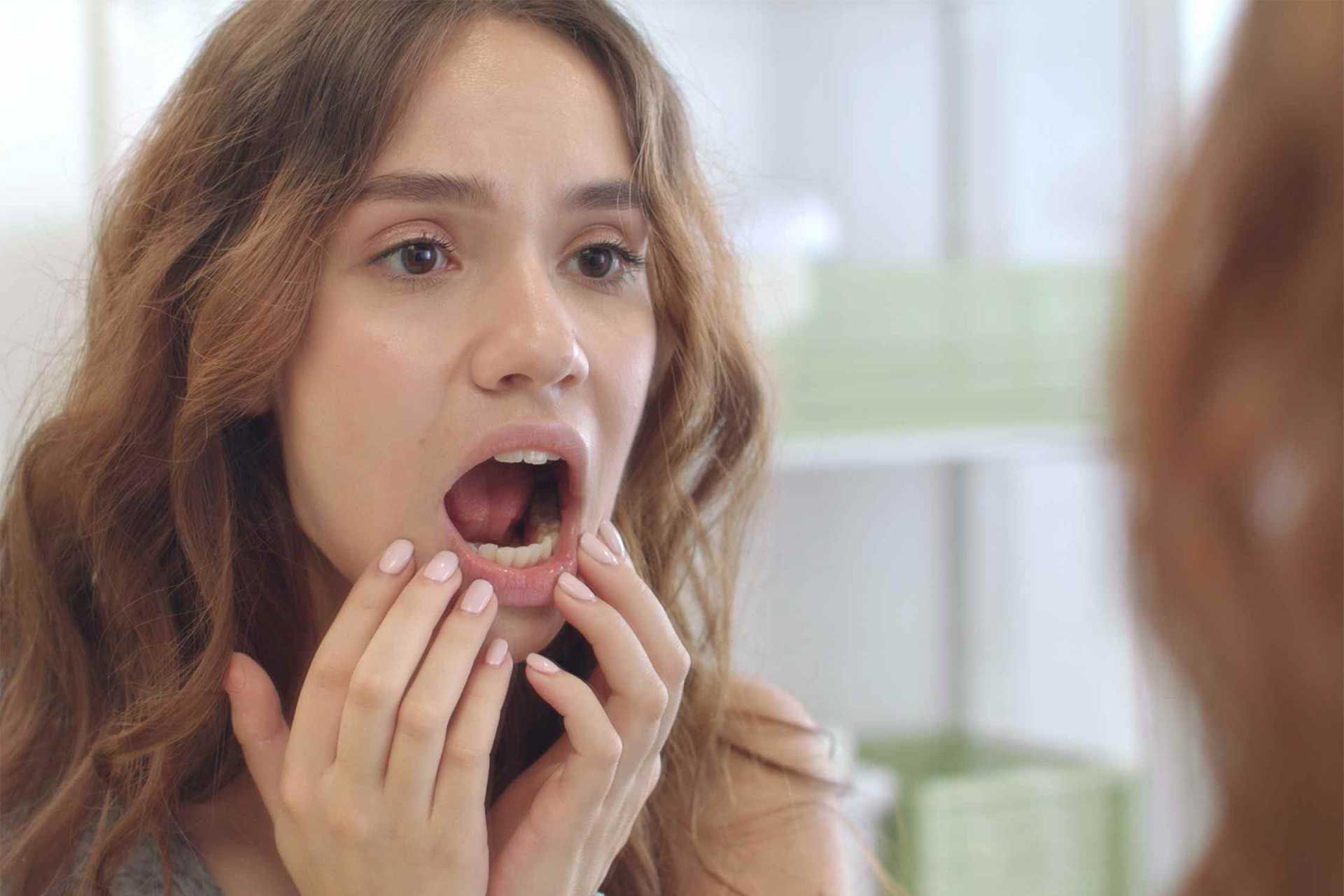 زن جوان با دهان باز به آینه نگاه می‌کنند