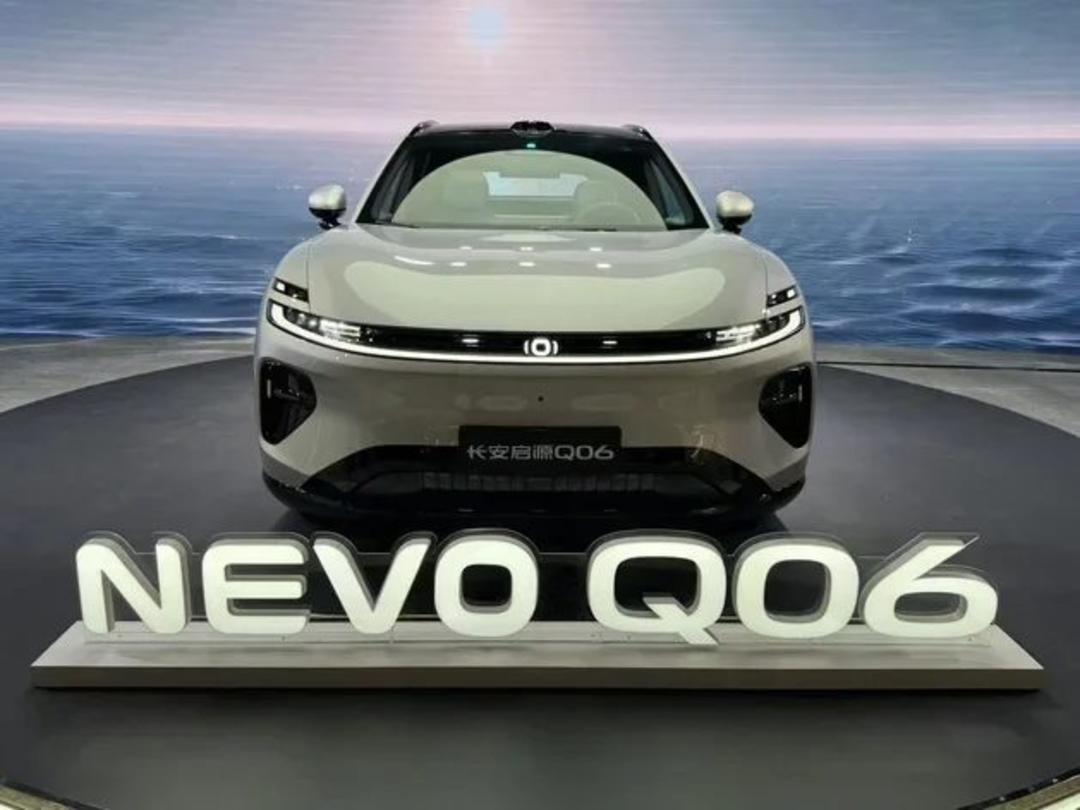 نمای جلوی خودروی برقی سفید رنگ مدل Nevo Q06 در یک نمایشگاه خودرو با پس‌زمینه دریایی.