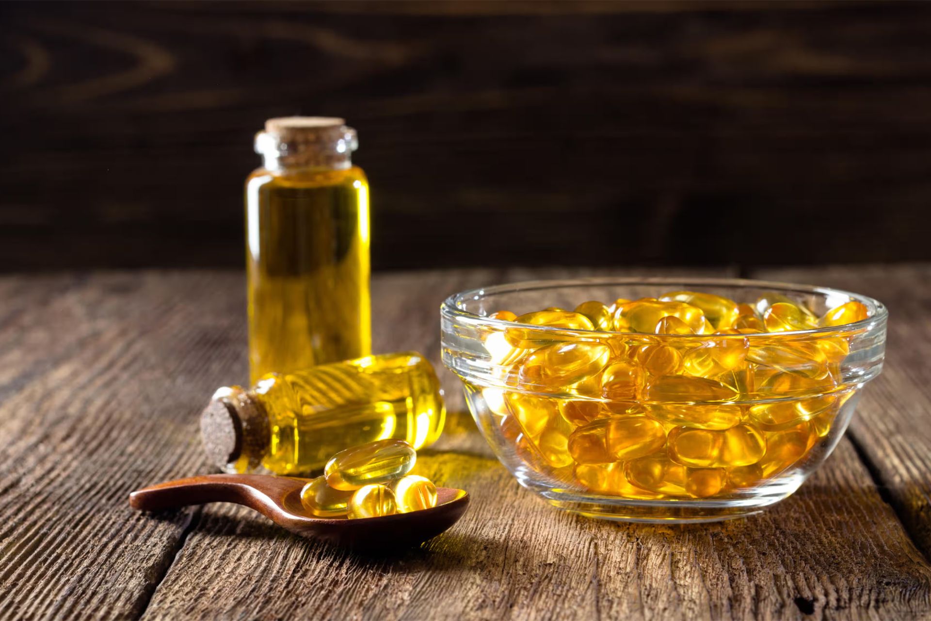 روغن امگا سه در بطری شیشه‌ای و به شکل کپسول در کاسه و در قاشق چوبی روی یک میز چوبی
