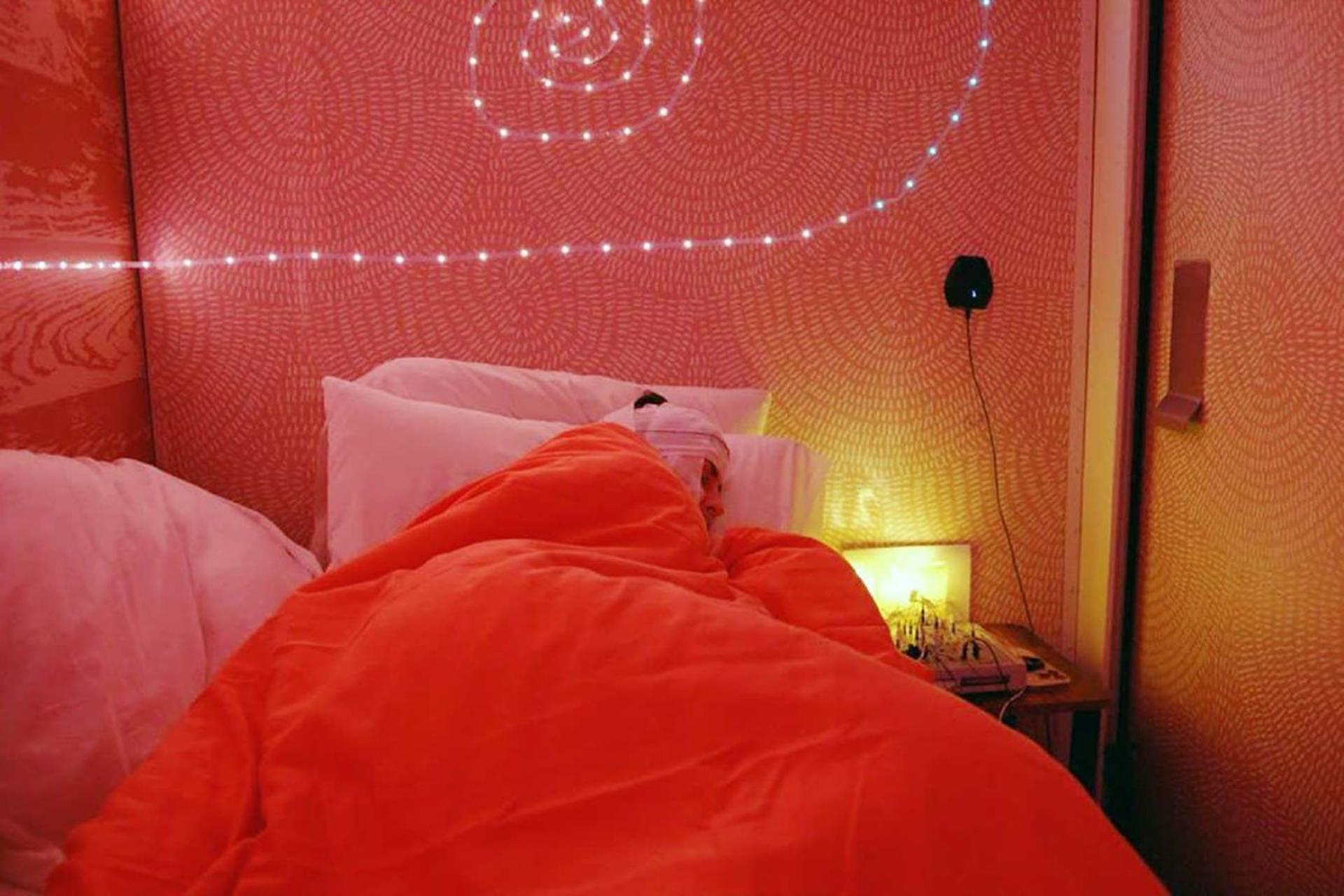 فرد داوطلب شرکت‌کننده در پژوهش مهندسی رویا که در طول آزمایش خواب با سرپوش در تخت با پتوی قرمز رنگ خوابیده است.