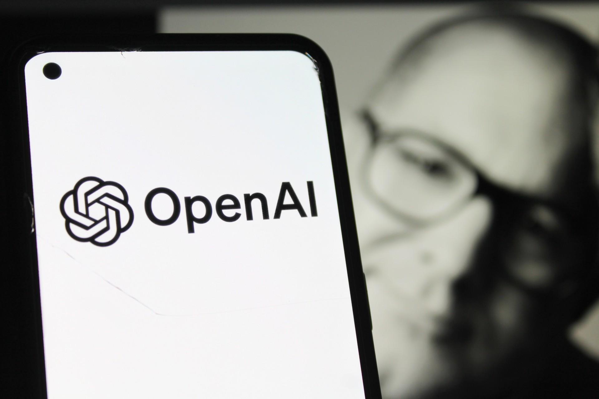 لوگو OpenAI روی صفحه‌ی سفید گوشی و چهره‌ی جانی آیو در پشت