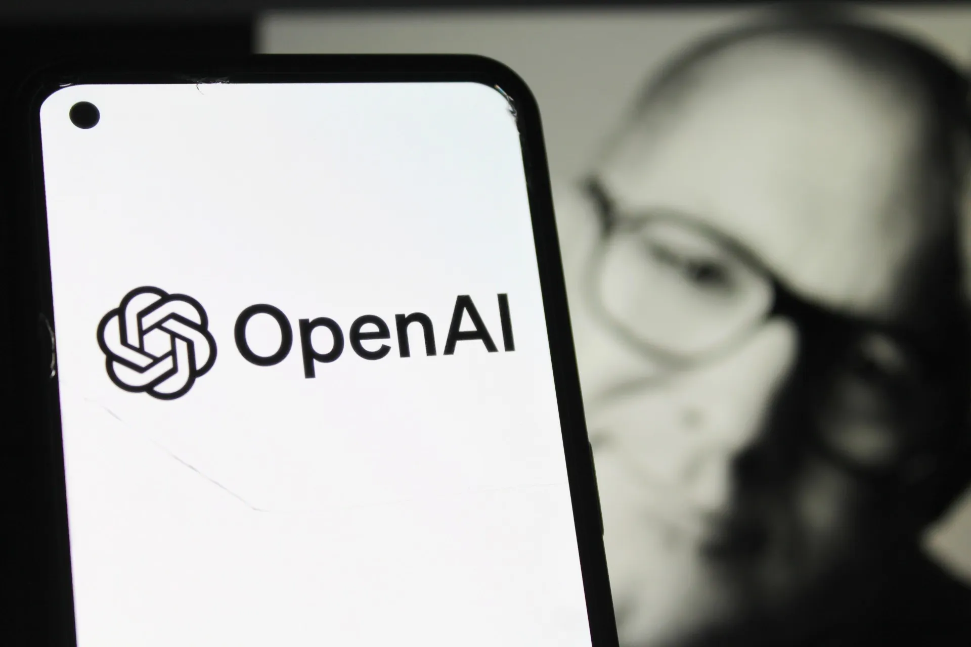 لوگو OpenAI روی صفحه‌ی سفید گوشی و چهره‌ی جانی آیو در پشت