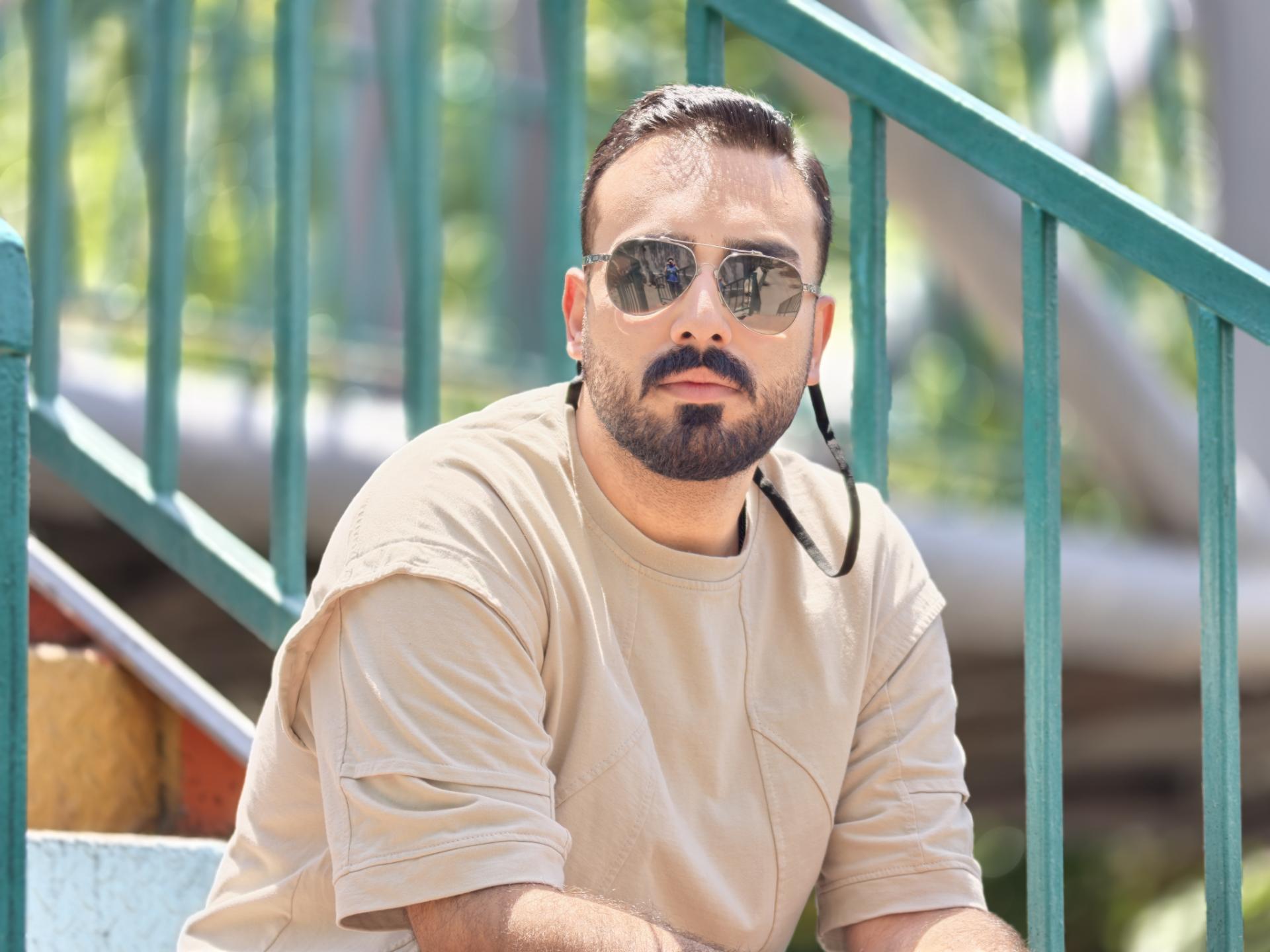 مردی با عینک آفتابی (Sunglasses) در فضای باز کنار نرده‌های سبز