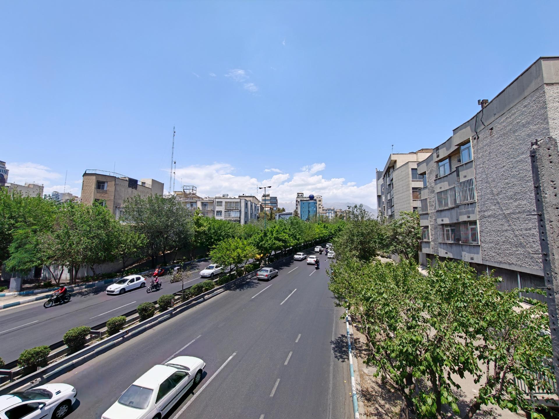 بلوار عریض شهری با خودروهای در حال حرکت و درختان در دو طرف