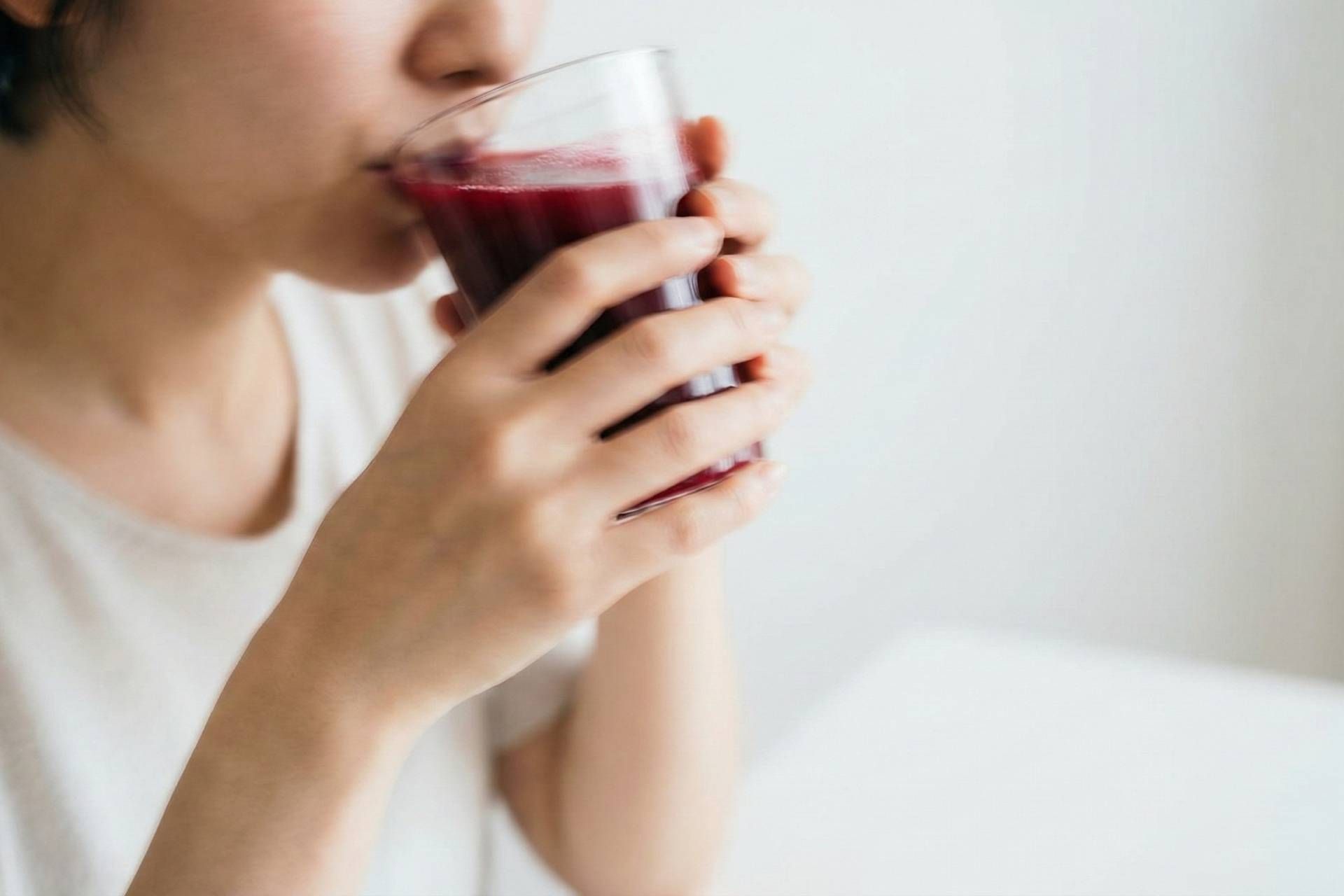 تصویرسازی تار از شخصی که در حال نوشیدن آبمیوه قرمز در یک محیط مینیمال سفید است.