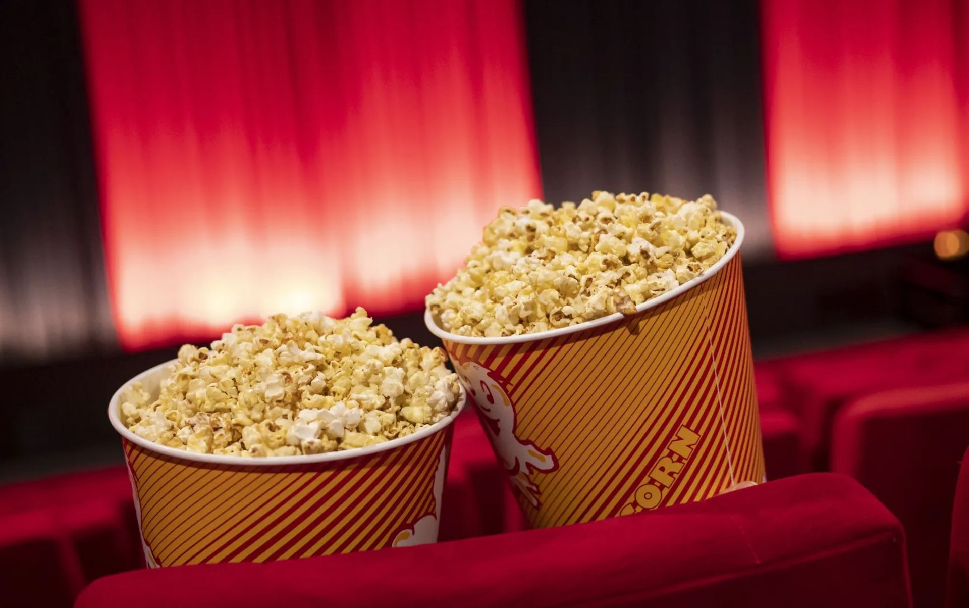 دو ظرف پاپ کورن در پس زمینه پرده سینما