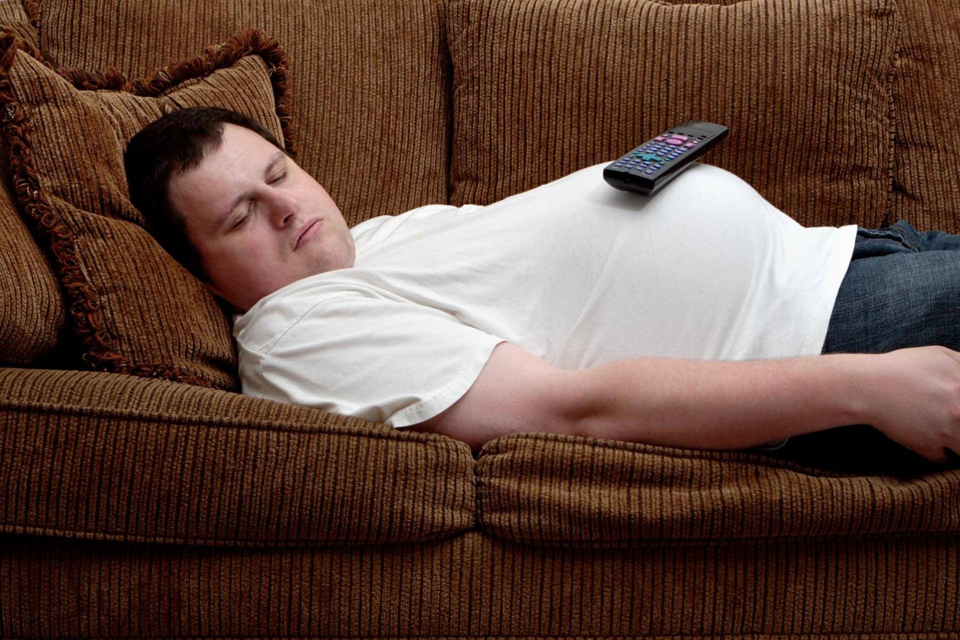 مرد جوان دارای اضافه‌وزن روی کاناپه دراز کشیده است