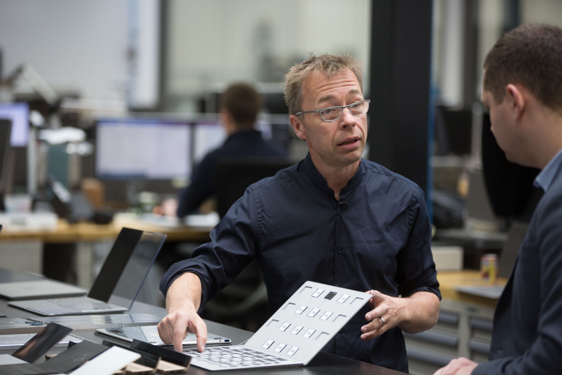 یک مرد میانسال در حال نشان‌دادن بدنه‌ی لپ‌تاپ به یک فرد دیگر