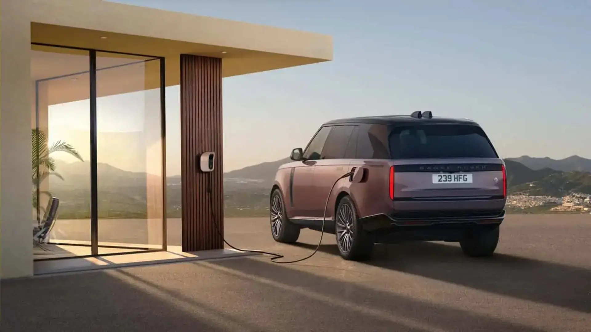 خودرو رنج‌روور الکتریک (Range Rover Electric) متصل به شارژر در مقابل یک ویلای مدرن