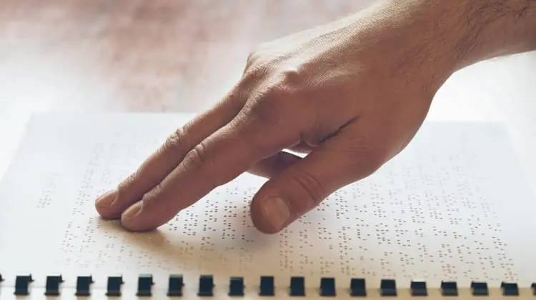 انگشتان فردی که در حال خواندن متن بریل (Braille) روی کاغذ است