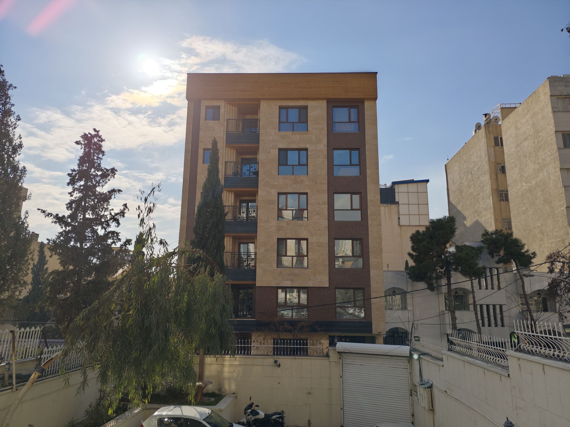 آسمان آفتابی با ساختمانی در روبرو و ماشین‌ها در پارکینگ