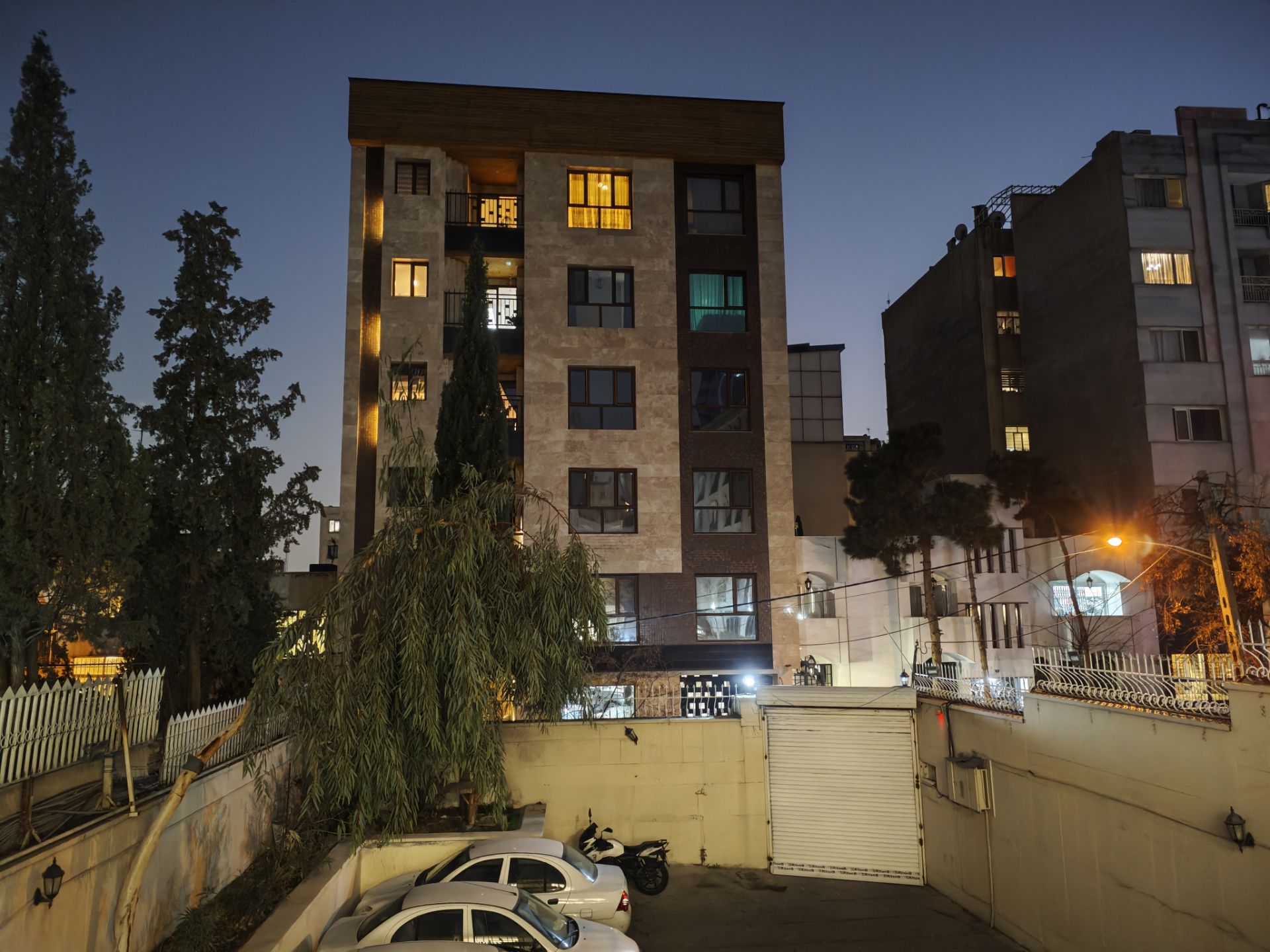 نمای ساختمان در روبرو و ماشین‌ها در حیاط