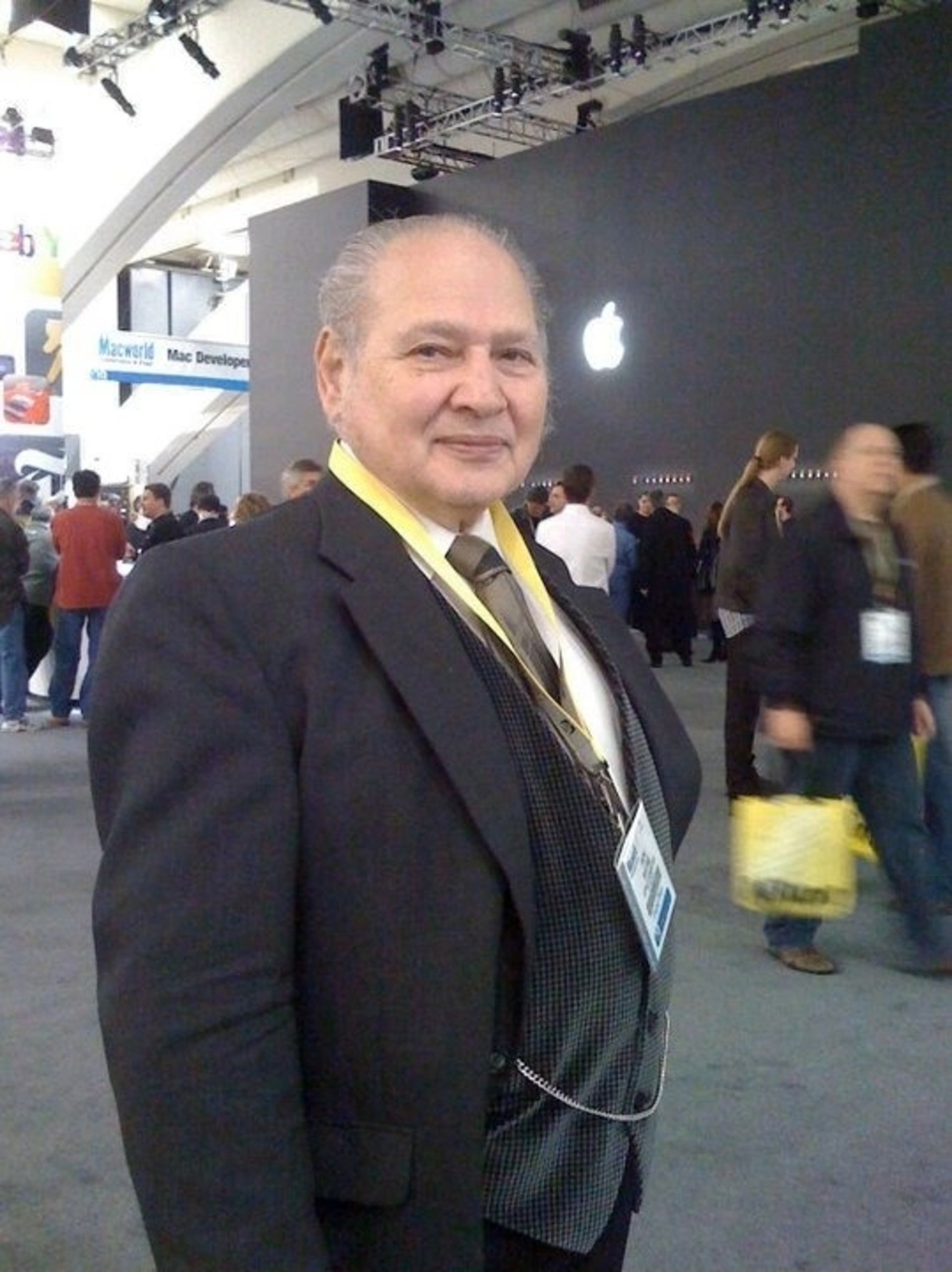 مرد میان‌سال با کت و شلوار مشکی روبه‌روی لوگو اپل